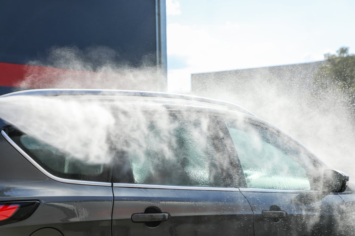 Car being thoroughly cleaned with a powerful high-pressure jet under radiant sunlight
