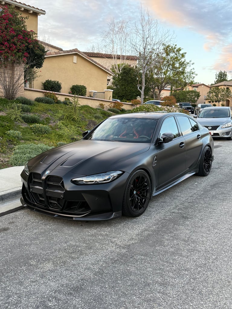 Black BMW M340i sedan parked in a residential driveway with beige house in background