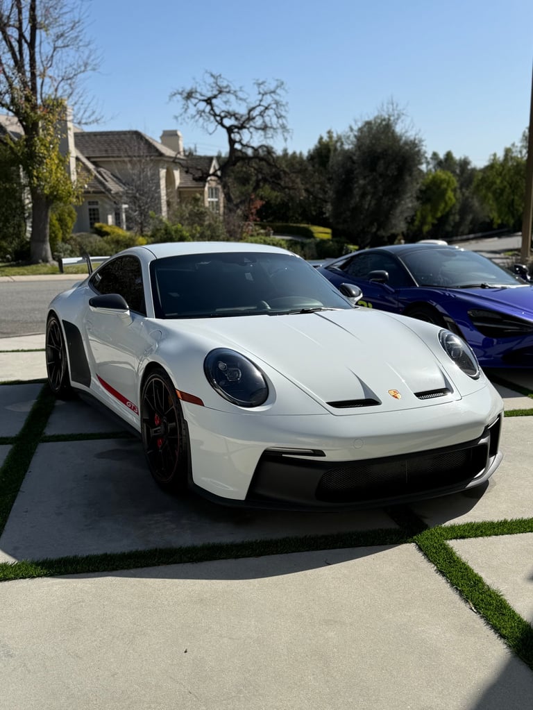 White Porsche 911 sports car parked on a residential driveway with a blue Porsche visible beside it