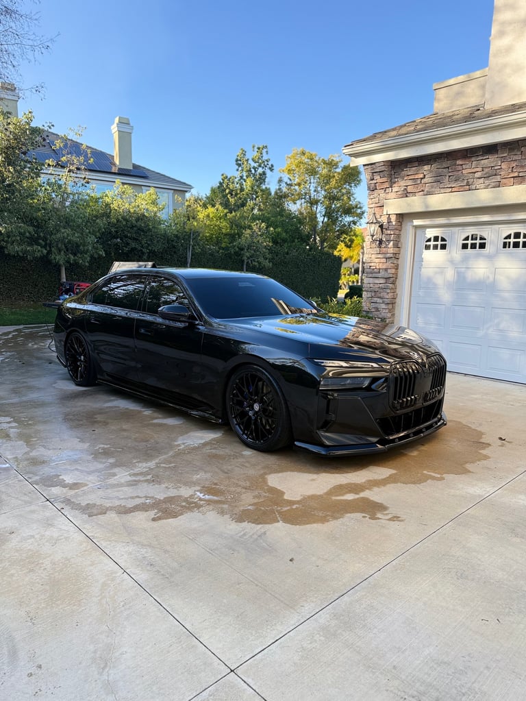 Black BMW sedan parked on driveway in front of stone house and white garage doors