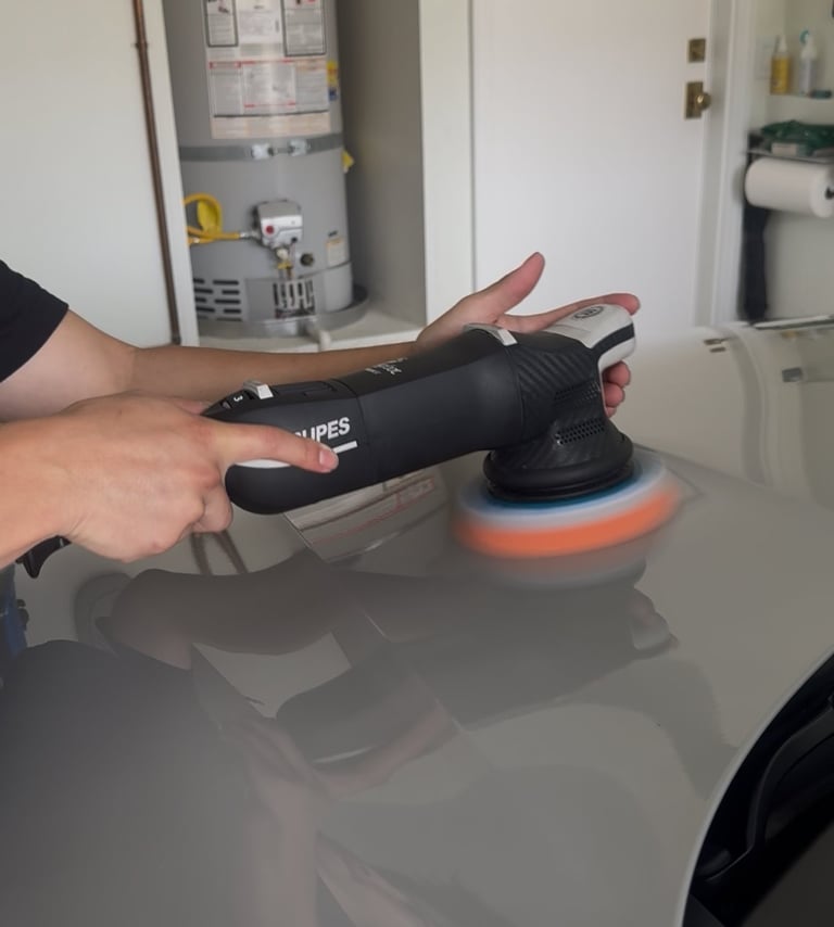 Person holding a black orbital polisher with orange polishing pad on a white countertop surface