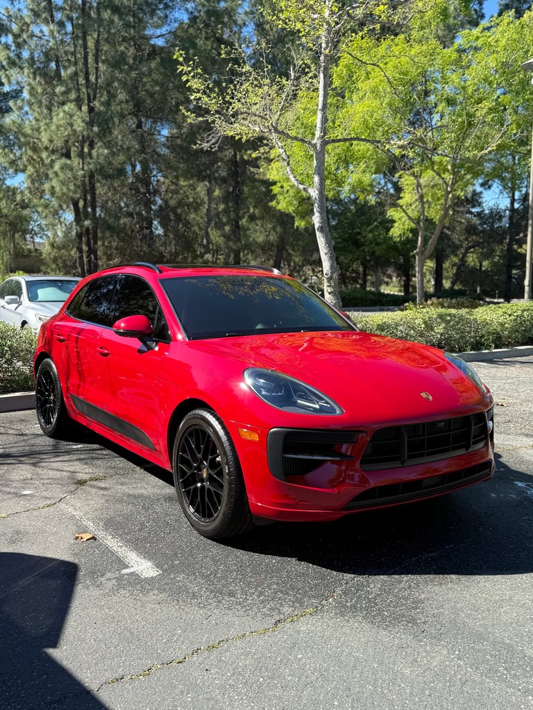 Bright red Porsche Macan sports SUV parked in a lot with trees and clear blue sky in the background