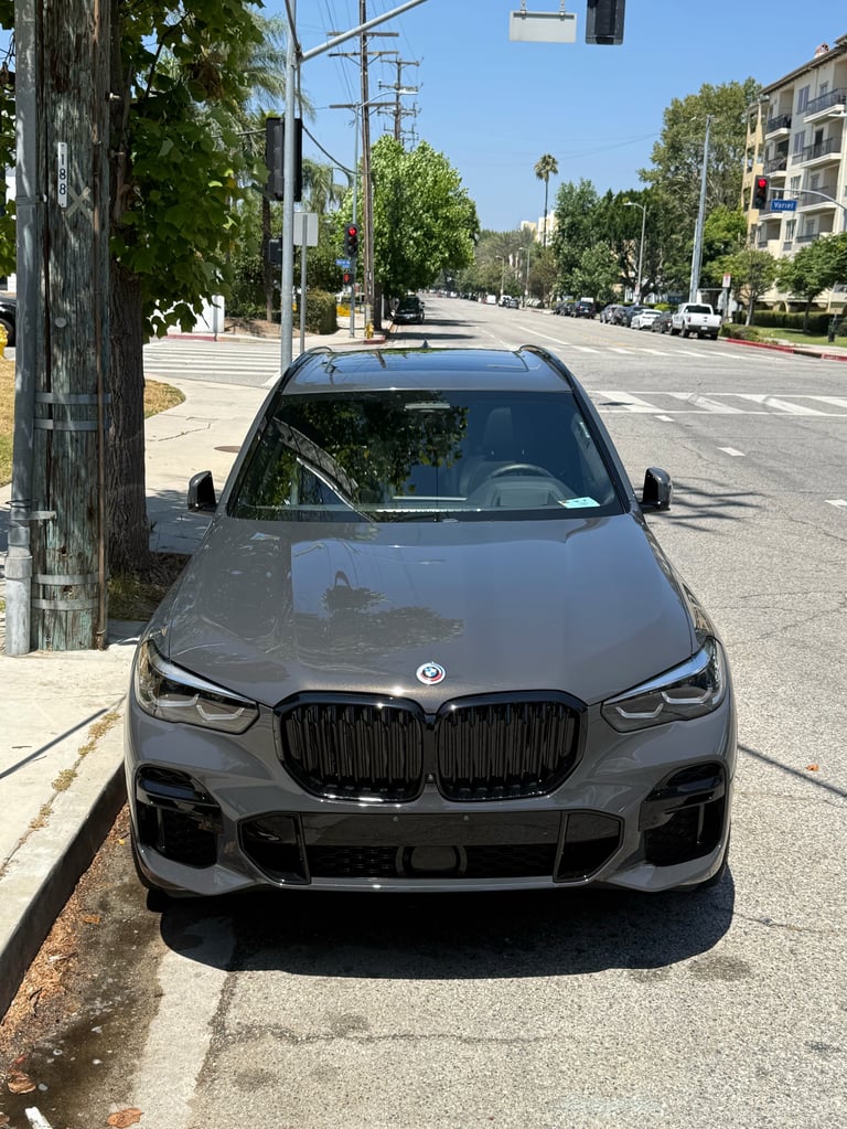 Gray BMW X3 SUV parked on a sunny residential street with trees and buildings visible